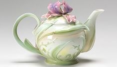 a ceramic teapot with flowers on the top is shown in front of a gray background