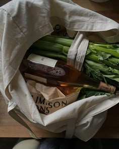 a bag filled with assorted veggies on top of a wooden table next to a bottle of wine