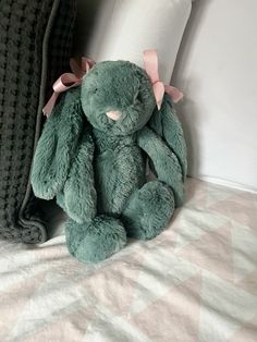 a green stuffed animal sitting on top of a bed next to a pillow and blanket