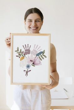 a woman holding up a framed painting with flowers on it