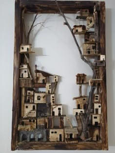 an art piece made out of wood with houses and trees in the middle, on a white wall