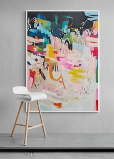 an abstract painting hangs on the wall next to a white chair