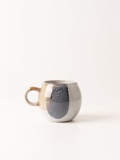 a white and grey cup with gold handles on a white surface, sitting in front of a plain background