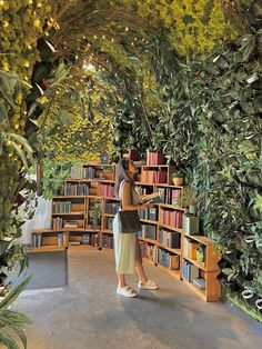 a woman standing in front of a bookshelf filled with lots of green plants