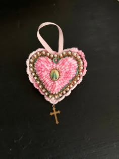 a pink heart shaped ornament with a cross hanging from it's side