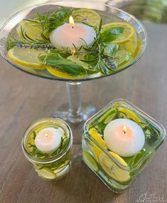 two candles sitting on top of a glass dish filled with lemon slices and herbs