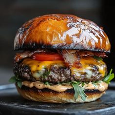 a cheeseburger with bacon, tomato and lettuce on a black plate