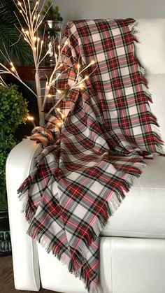 a plaid blanket draped over a white couch next to a christmas tree with lights on it