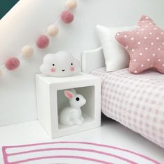 a white bed with pink and white decor on the headboard next to a small rabbit figurine