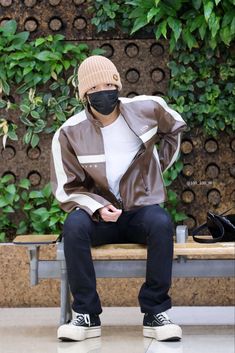 a man wearing a face mask sitting on a bench with his hands in his pockets