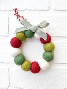 a felt wreath hanging on a brick wall with a ribbon tied around it and some balls in the middle