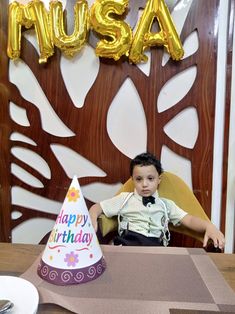 a young boy sitting at a table in front of a birthday hat with the word musa on it