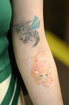 a woman's arm with two cats on it and one cat has a bow around its neck