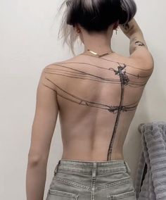 a woman with tattoos on her back standing in front of a wall