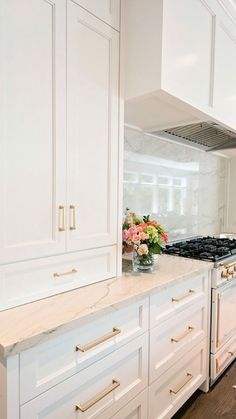 a white kitchen with marble counter tops and gold pulls on the cabinets in front of the stove