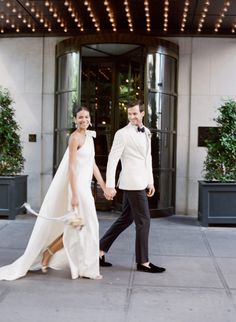 a bride and groom walking their dog in front of the hotel entrance with lights on