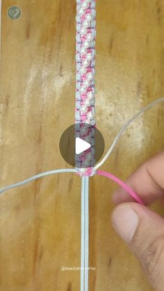 someone is making a piece of string with pink and white beads on it, while another hand holds the string in front of them