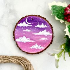 a purple and white painted wooden ornament next to some holly wreaths on a marble surface