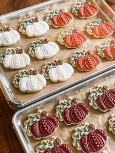 two trays filled with decorated cookies sitting on top of a wooden table next to each other