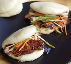 two buns filled with meat and vegetables on a black plate