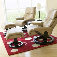 two reclining chairs and a footstool on a rug in front of a window