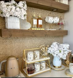 a kitchen counter topped with lots of dishes and vases filled with white flowers on top of shelves