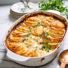 a casserole dish with potatoes and parsley in it on a marble table