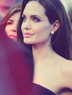 a close up of a woman with long dark hair and wearing diamond earrings