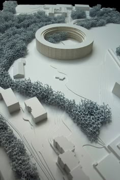 an architectural model of a circular building surrounded by trees and bushes on a white surface