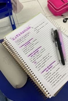 a notepad and pen sitting on top of a blue chair next to a pink purse