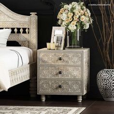 a white bed sitting next to a vase with flowers on top of it