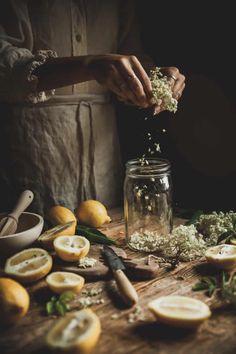 a person is sprinkling flowers into a jar filled with lemons and herbs