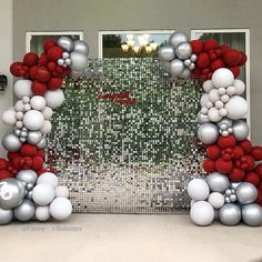 an arch made out of balloons and silver and red balls in front of a door