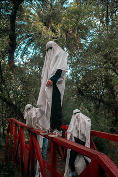 two people dressed in white and black standing on a red bridge with trees behind them