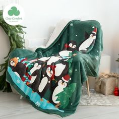 a green blanket with penguins on it sitting next to a christmas tree and potted plant