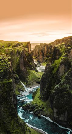 a river flowing through a lush green hillside covered in grass next to tall rocky cliffs