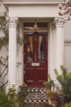 a red front door with two potted plants on either side and a checkerboard floor