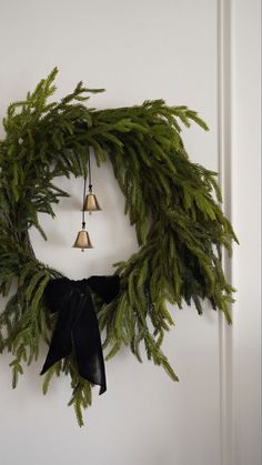 a wreath with bells hanging from it's side and evergreen leaves on the front