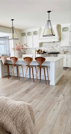 a kitchen with white cabinets and wooden flooring next to a dining room table filled with chairs