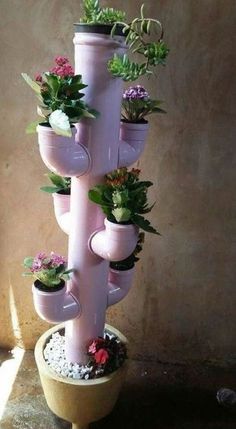 a tall pink planter with potted plants on it's sides and hanging from the top