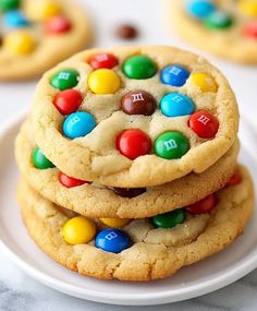 cookies with m & m candies on top are stacked on a white plate and ready to be eaten