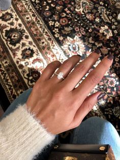 a woman's hand with a diamond ring on her finger, sitting in front of a rug