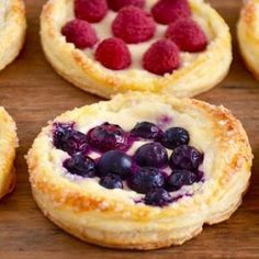 several pastries with berries and blueberries in them on a wooden surface, ready to be eaten