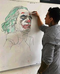 a man drawing on a white board with a clown face drawn on it and another person standing next to him