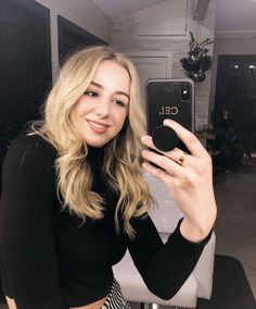 a woman taking a selfie with her cell phone in front of the camera and wearing a black top