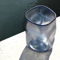 a glass cup sitting on top of a cement slab next to a body of water