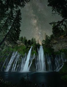 the night sky over a waterfall with stars above it and some trees in the foreground