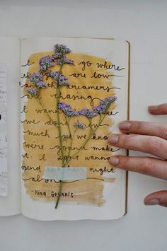 a hand holding an open book with writing on it and flowers in the pages next to each other