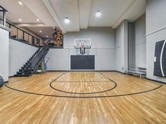 an indoor basketball court with hard wood flooring and stairs leading up to the upper level