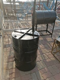 a large black barrel sitting on top of a brick floor next to a metal structure